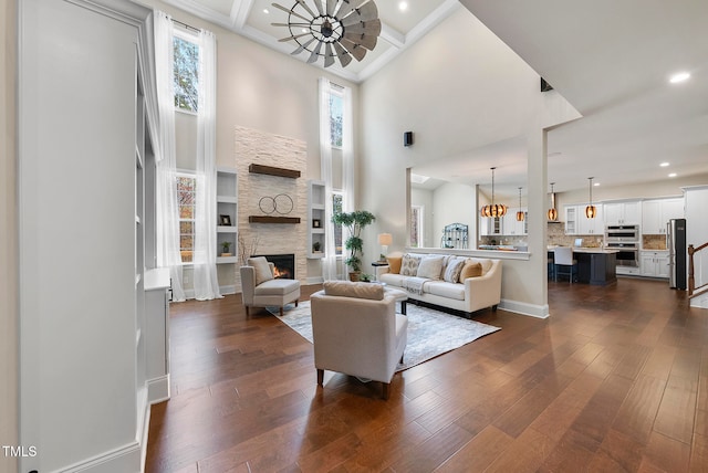 living room with a towering ceiling, dark hardwood / wood-style floors, a stone fireplace, and a notable chandelier