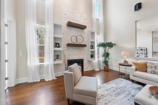 living room featuring built in shelves, dark hardwood / wood-style floors, a stone fireplace, and a towering ceiling