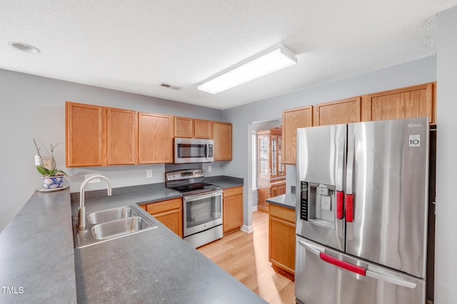 kitchen with sink, stainless steel appliances, a textured ceiling, and light wood-type flooring