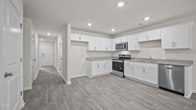 kitchen featuring sink, appliances with stainless steel finishes, light stone countertops, white cabinets, and light wood-type flooring