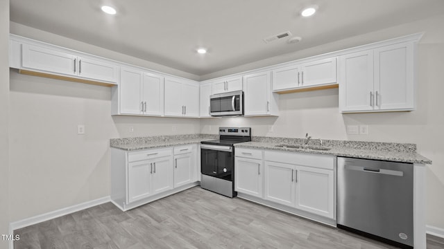 kitchen featuring sink, appliances with stainless steel finishes, light stone countertops, light hardwood / wood-style flooring, and white cabinets