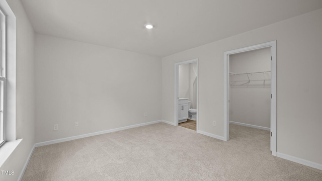 unfurnished bedroom with ensuite bathroom, light colored carpet, a closet, and a spacious closet