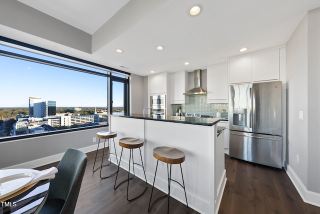 kitchen with appliances with stainless steel finishes, dark hardwood / wood-style flooring, wall chimney exhaust hood, white cabinetry, and a kitchen island