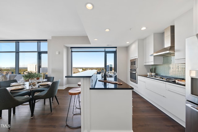 kitchen with a breakfast bar, stainless steel appliances, white cabinetry, and wall chimney exhaust hood