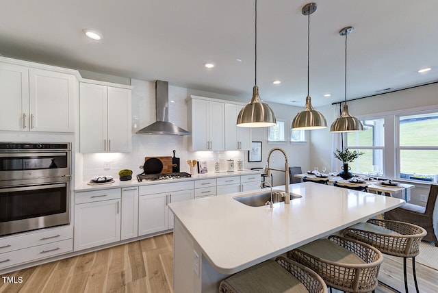 904 Delano Dr, Knightdale, NC 27545 - kitchen featuring a sink, wall chimney exhaust hood, stainless steel appliances, light wood-style flooring, and a kitchen bar