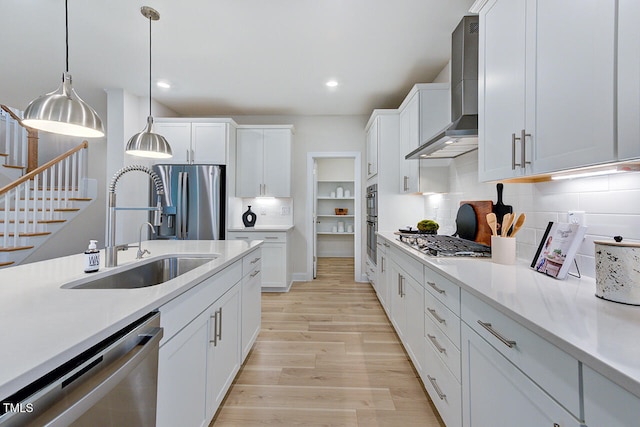 kitchen featuring appliances with stainless steel finishes, wall chimney exhaust hood, sink, pendant lighting, and white cabinetry