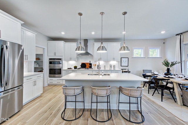 kitchen with white cabinetry, hanging light fixtures, wall chimney exhaust hood, and stainless steel appliances