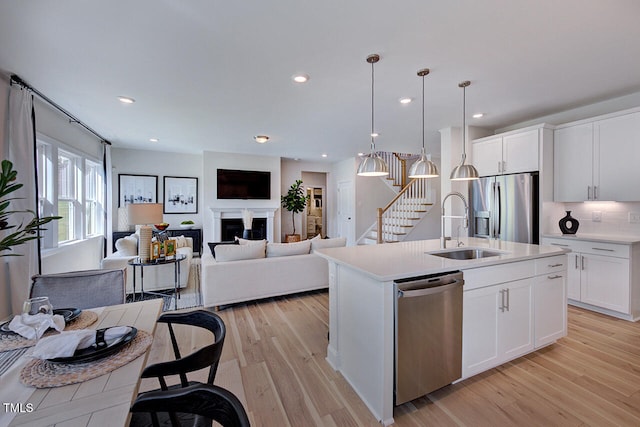 kitchen featuring pendant lighting, white cabinets, a center island with sink, light hardwood / wood-style flooring, and appliances with stainless steel finishes