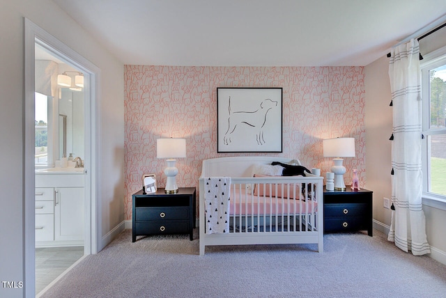 bedroom with carpet flooring, ensuite bathroom, a crib, and sink