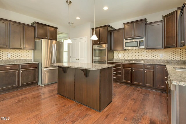 kitchen with a center island, dark hardwood / wood-style floors, light stone countertops, decorative light fixtures, and stainless steel appliances