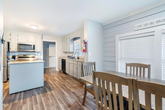 kitchen with stainless steel appliances, wooden walls, sink, hardwood / wood-style flooring, and white cabinets