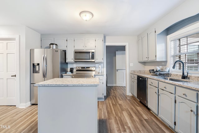 kitchen with light stone countertops, sink, appliances with stainless steel finishes, a kitchen island, and light wood-type flooring