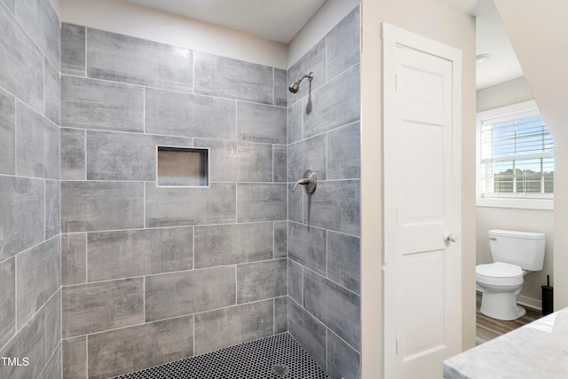 bathroom with hardwood / wood-style flooring, toilet, and tiled shower