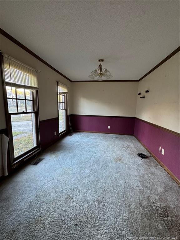 empty room with a textured ceiling, ornamental molding, and carpet floors