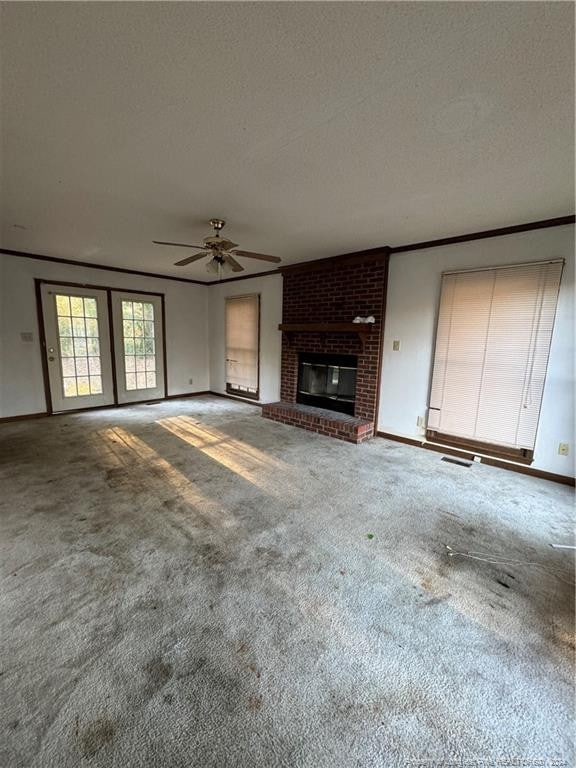 unfurnished living room featuring carpet flooring, a textured ceiling, ceiling fan, crown molding, and a fireplace