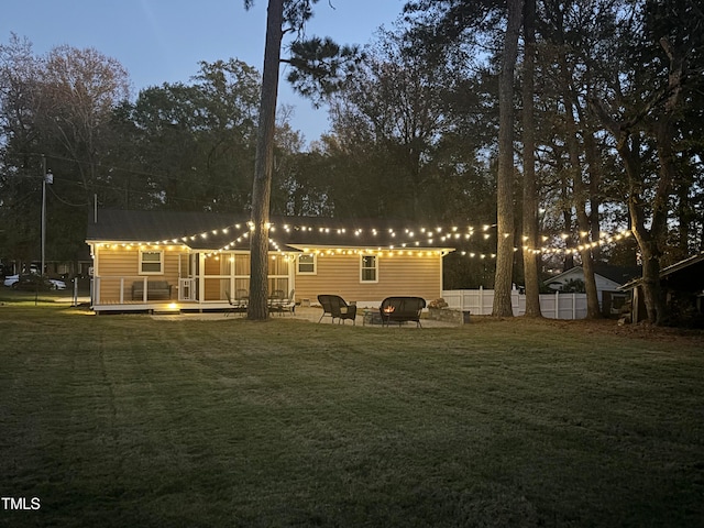 back house at dusk featuring a lawn, a patio, and a deck