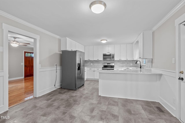 kitchen featuring kitchen peninsula, tasteful backsplash, stainless steel appliances, crown molding, and white cabinets