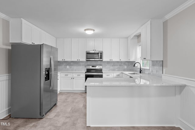 kitchen with kitchen peninsula, appliances with stainless steel finishes, ornamental molding, sink, and white cabinetry