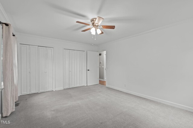 unfurnished bedroom featuring ceiling fan, crown molding, light carpet, and two closets