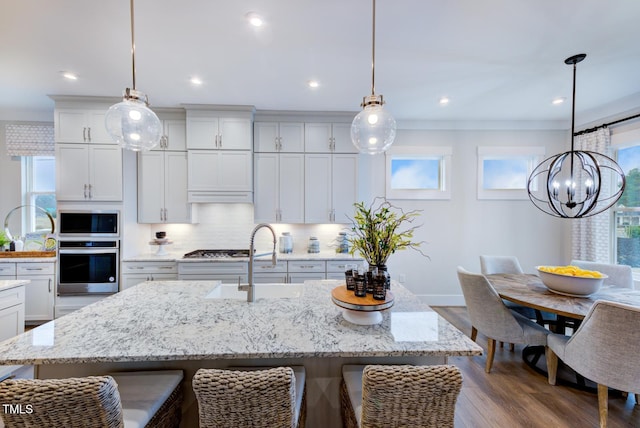 kitchen with white cabinetry, appliances with stainless steel finishes, a kitchen island with sink, and hanging light fixtures