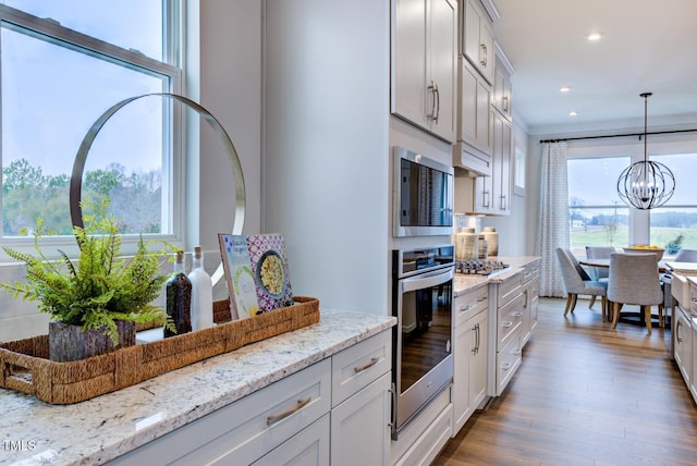 kitchen featuring decorative light fixtures, a notable chandelier, light stone counters, stainless steel appliances, and dark wood-type flooring