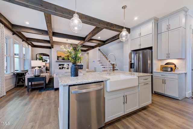 kitchen featuring pendant lighting, sink, appliances with stainless steel finishes, white cabinetry, and a center island with sink