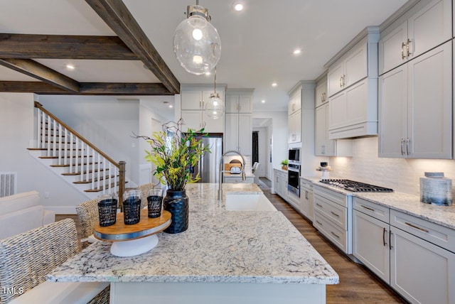 kitchen featuring sink, decorative light fixtures, a large island with sink, appliances with stainless steel finishes, and light stone countertops