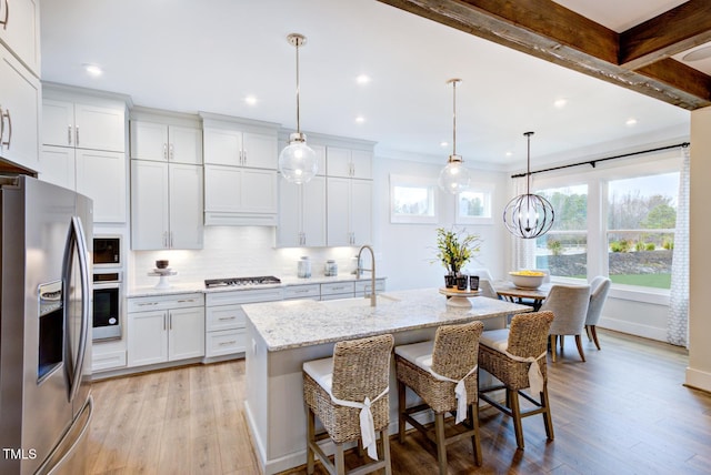 kitchen featuring pendant lighting, an island with sink, white cabinetry, a kitchen breakfast bar, and stainless steel appliances