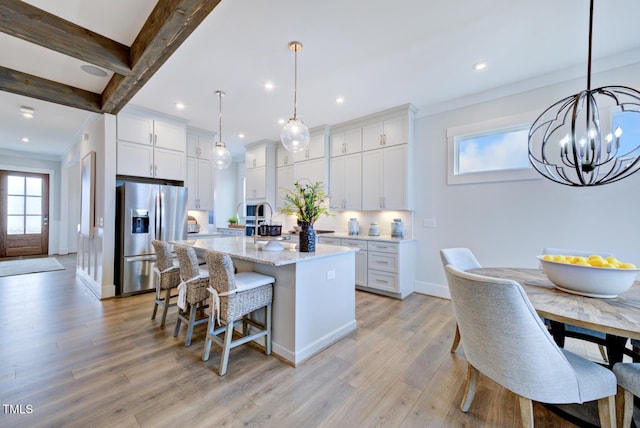 kitchen featuring white cabinetry, an island with sink, pendant lighting, and stainless steel fridge