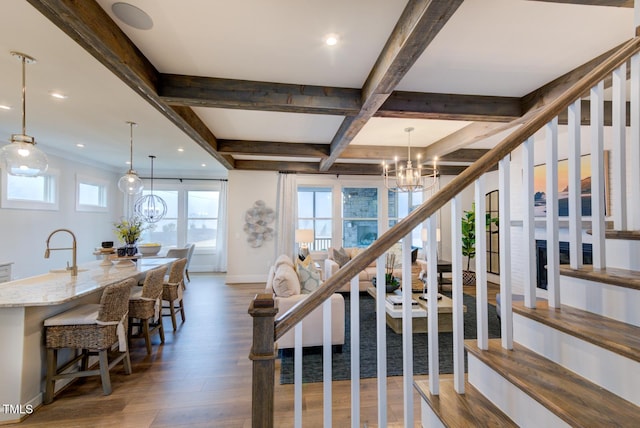 staircase featuring sink, beam ceiling, coffered ceiling, wood-type flooring, and a chandelier