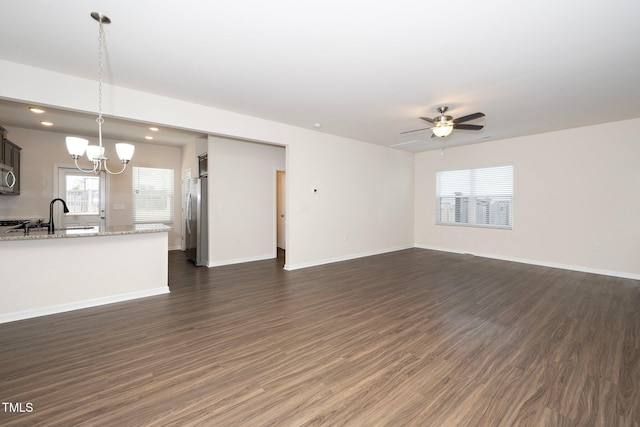 unfurnished living room featuring ceiling fan with notable chandelier, sink, and dark hardwood / wood-style flooring