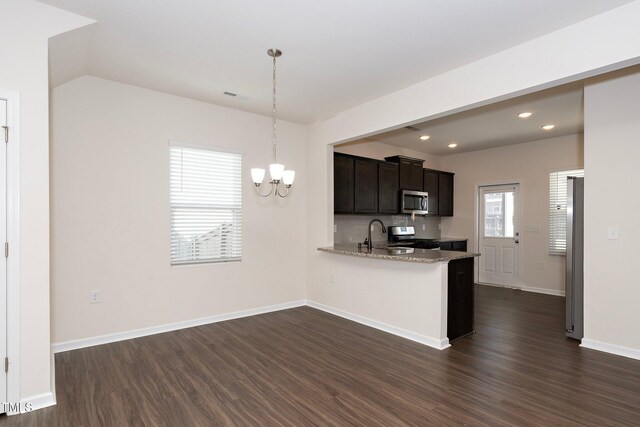 kitchen with stainless steel appliances, hanging light fixtures, dark hardwood / wood-style floors, kitchen peninsula, and light stone counters