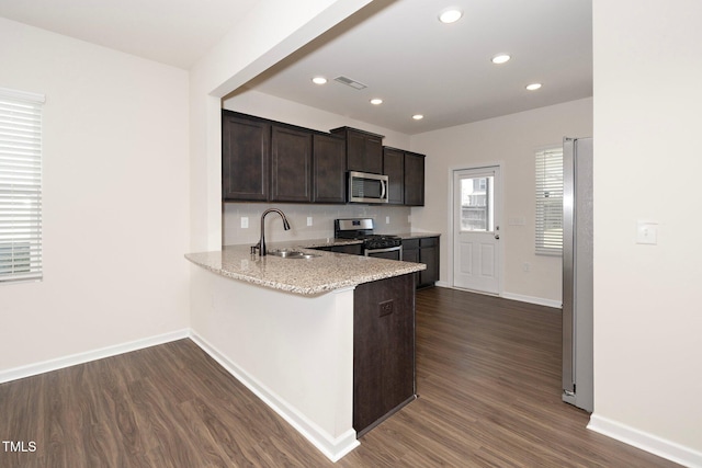 kitchen with appliances with stainless steel finishes, dark wood-type flooring, sink, kitchen peninsula, and light stone counters