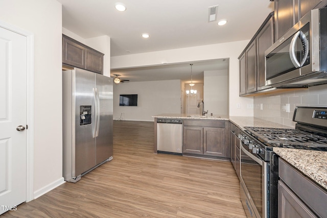 kitchen with light stone countertops, kitchen peninsula, pendant lighting, backsplash, and stainless steel appliances