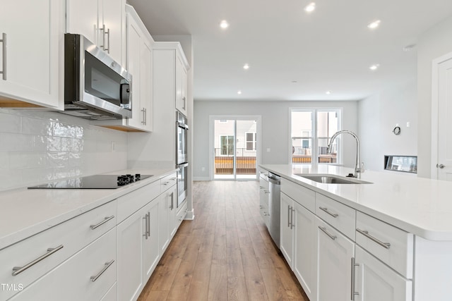 kitchen with light hardwood / wood-style flooring, white cabinetry, an island with sink, appliances with stainless steel finishes, and tasteful backsplash