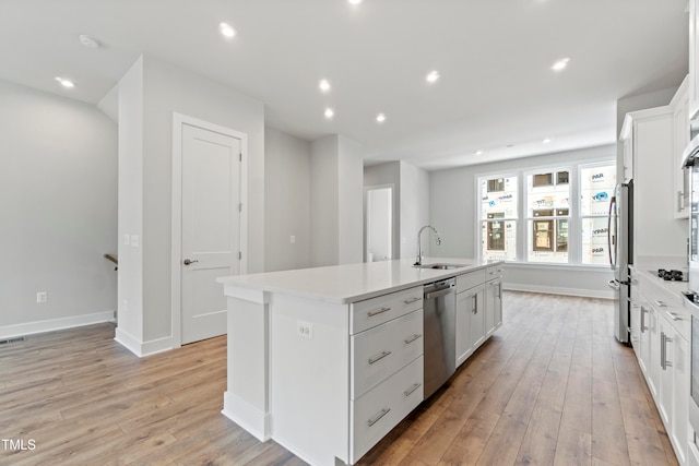 kitchen featuring appliances with stainless steel finishes, light wood-type flooring, white cabinetry, and an island with sink