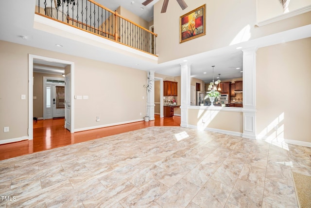 unfurnished living room with a high ceiling, ceiling fan with notable chandelier, and ornate columns