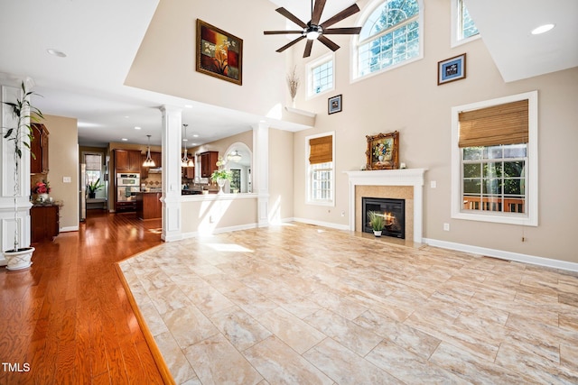 unfurnished living room with ceiling fan, light hardwood / wood-style floors, ornate columns, and a high ceiling