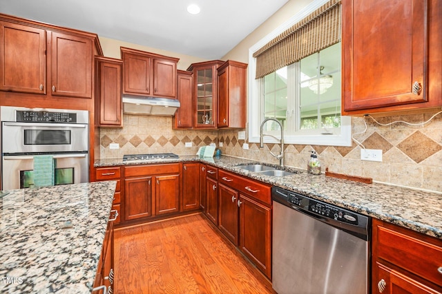 kitchen featuring backsplash, sink, light hardwood / wood-style flooring, light stone countertops, and stainless steel appliances