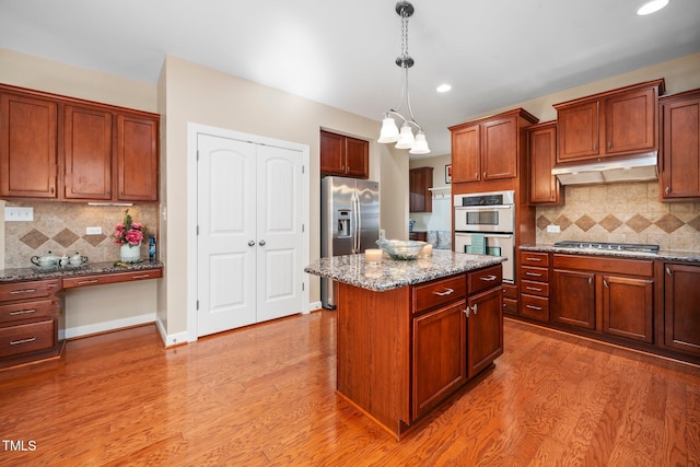 kitchen with decorative backsplash, a center island, light stone countertops, and appliances with stainless steel finishes