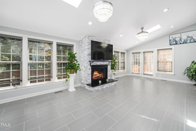 unfurnished living room with a chandelier, lofted ceiling with skylight, and a stone fireplace