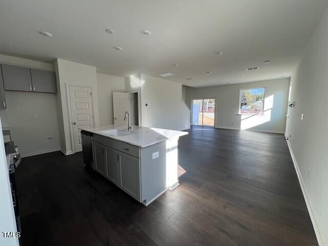 kitchen with dark wood-type flooring, a kitchen island with sink, gray cabinets, light countertops, and a sink