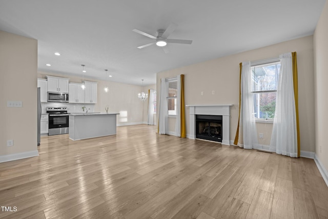 unfurnished living room with ceiling fan with notable chandelier and light hardwood / wood-style flooring