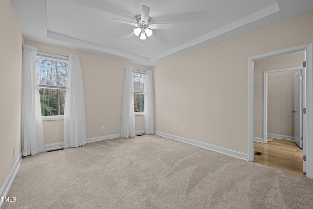 carpeted empty room featuring a wealth of natural light, a raised ceiling, and ceiling fan