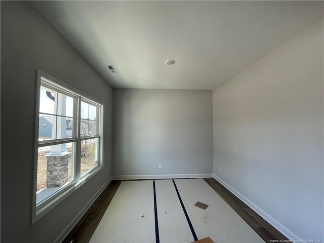 spare room featuring dark wood-style floors, visible vents, and baseboards