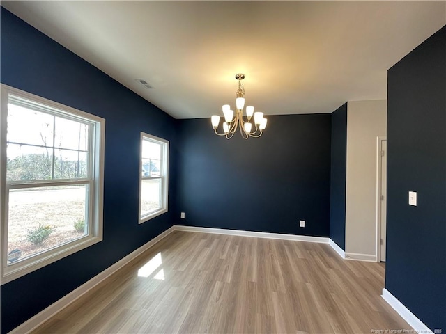 empty room with visible vents, baseboards, a chandelier, and light wood finished floors