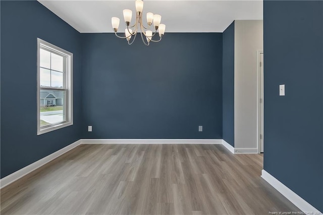 spare room featuring baseboards, wood finished floors, and a chandelier