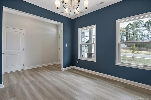 unfurnished room with visible vents, baseboards, wood finished floors, and an inviting chandelier