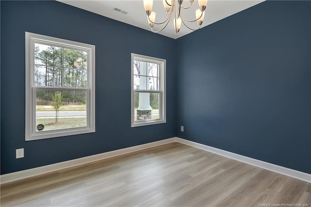 empty room with baseboards, visible vents, wood finished floors, and a notable chandelier