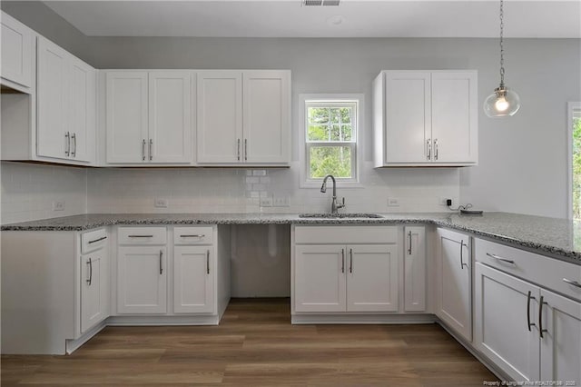 kitchen featuring a sink, light stone counters, tasteful backsplash, and white cabinetry